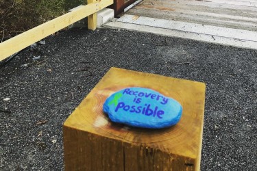 Recovery is Possible painted on a rock with a green ribbon for mental health awareness
